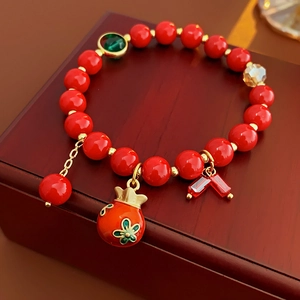 Détail du bracelet en perles rouges avec charm grenade et accents dorés sur bois