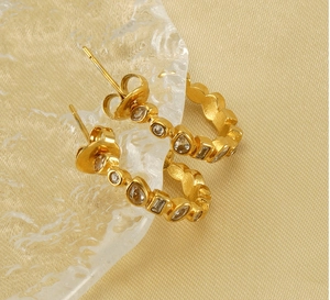 Detail of 18k gold U-shaped earrings with multi-shape zircon stones on a silk fabric