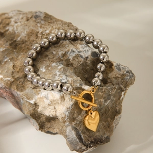 Silver bead bracelet with gold OT clasp and heart charm on a textured rock surface