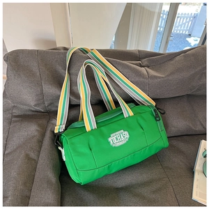 Close-up of green cylindrical sports bag featuring striped straps on a gray sofa