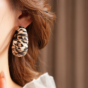 Close-up of a model wearing leopard print C-shaped hoop earrings with a vintage texture