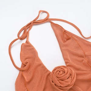 Detail of caramel ruffled halter dress featuring a 3D floral accent and ribbed metallic fabric