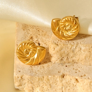 Detail view of 18K gold plated conch stud earrings on a textured beige stone background