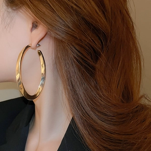 Close-up of model wearing large gold oval hoop earrings with a polished mirror finish