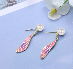 Macro shot of gold long drop earrings with white pearl and pink-purple gradient wings