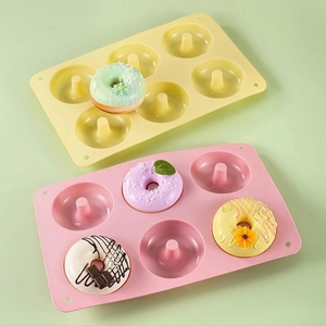 Pink and yellow six-cavity silicone donut molds with fresh baked donuts on green background