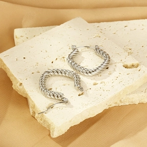 Close-up of silver twist rope hoop earrings on a textured stone and champagne satin