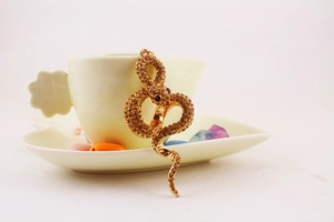 Macro view of golden snake keychain with brown rhinestones and red gem eyes on a ceramic cup