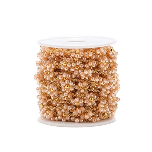 Macro detail of 1.5mm gold plated flat chain with woven peach crystal flowers on a roll