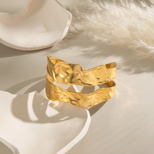 Macro detail of gold textured wavy metal cuff bracelet on an artistic stone pedestal