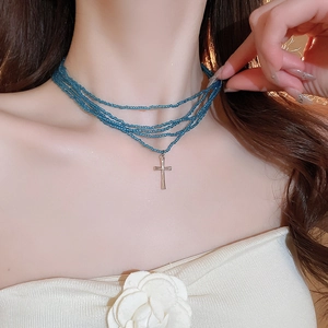 Multi-layer blue beaded necklace featuring a silver cross pendant on a female model