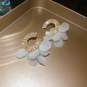 Macro view of C-shape zircon earrings with white petal tassels on a golden metal tray