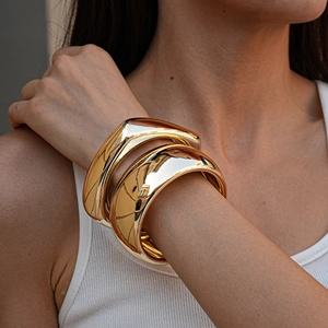 Close-up of chunky polished gold acrylic cuffs showing mirror finish on model's wrist