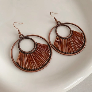 Detail of vintage bronze round hollow earrings with brown cotton tassels on white ceramic tray