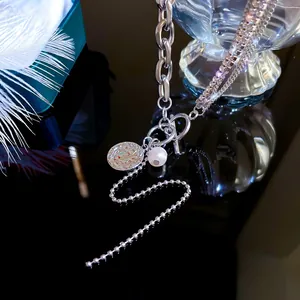 Detail of layered silver necklaces with OT buckle, coin pendant and pearls on black surface
