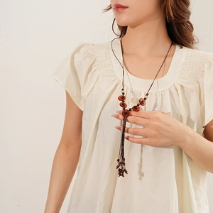 Detail of bohemian long necklace with dark brown wooden beads and tassel on a beige top