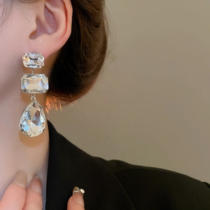 Macro shot of long sparkling rhinestone earrings with square and teardrop crystal pendants