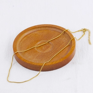 Detail of adjustable gold snake chain necklace with lobster clasp on wooden tray