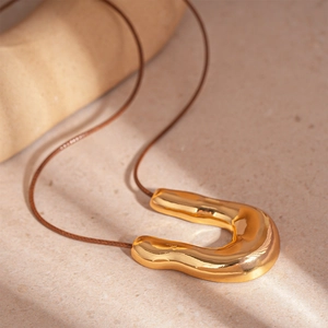 Detail of a liquid metal gold U-shaped pendant on a brown cord against stone