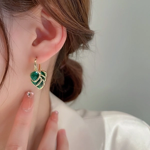 Detailed close-up of gold butterfly earrings with green stones worn by a model