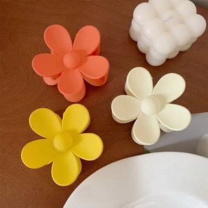 Detail of matte floral hair claws in orange, yellow, and cream on a wooden surface