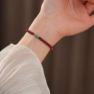 Close-up of cinnabar beaded bracelet with turquoise bead and golden accents on wrist