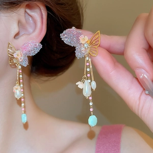 Close-up of butterfly earrings with pearls and purple crystals on a golden tassel base