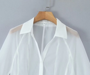 Detail of white V-neck sheer textured fabric shirt dress with long sleeves on a wooden hanger
