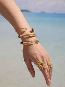 Golden flower bracelet and sun ring set with sparkling zircon on a bright beach background