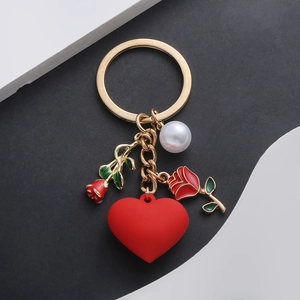 Close-up of gold keychain with red heart, roses, and a white pearl on a modern backdrop