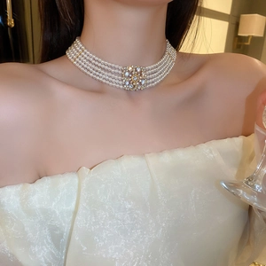 Close-up of layered pearl choker with gold floral rhinestone clasp worn by a model