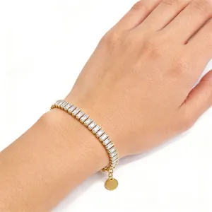 Gold-tone tennis bracelet with baguette-cut zircon stones and a round gold tag charm