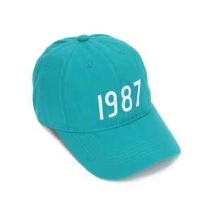 Close-up of teal cotton baseball cap with high-quality white 1987 number embroidery