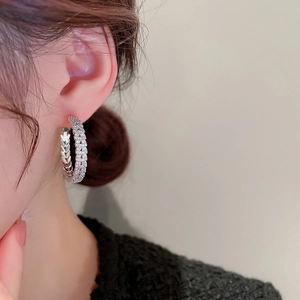 Close-up of a silver hoop earring with zircon wheat leaf patterns on a model's ear
