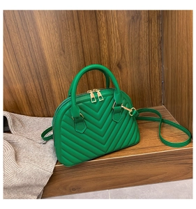 Green shell-shaped handbag with V-quilted pattern and gold zipper on a wood background