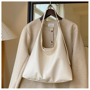 Detail of a minimalist off-white PU leather hobo shoulder bag hanging on a coat hanger