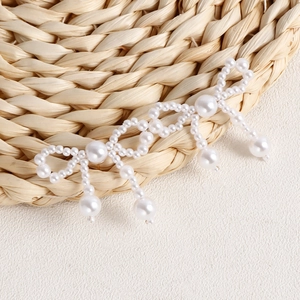 Detail of handmade white pearl bow earrings with elegant fringe tassels on a woven mat
