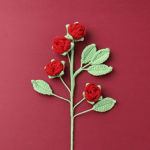 Flat lay of four handmade red crochet roses and six green leaves on a dark red background