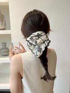 Detailed view of cream hair scrunchie with rose embroidery, lace trim, and pearl bow