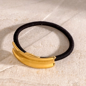 Close-up of minimalist black elastic hair tie with polished gold metal buckle on marble