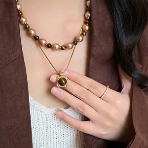 Detail of layered 18K gold tiger eye necklace and pearl jewelry on a model