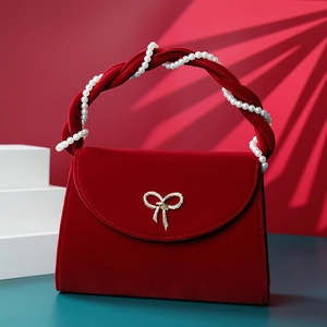 Detail of red velvet handbag with pearl handle and golden bow hardware on the front