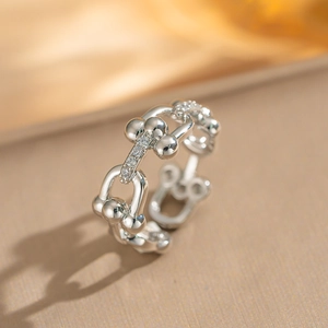 Macro detail of silver U-link chain ring with zircon pave on warm silk background