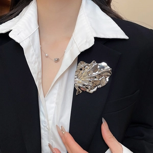 Detail shot of a silver pleated leaf brooch styled on a professional black blazer