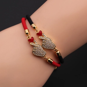 Close-up of woven couple bracelets with gold heart charms and cubic zirconia details
