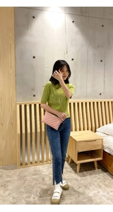 Detailed view of a pink quilted chain handbag held by a model in a minimalist bedroom setting