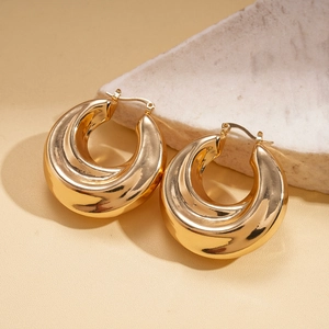 Detailed close-up of chunky gold hoop earrings with polished finish on marble surface