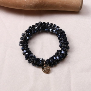 Detail of black crystal beaded hair tie with gold round metal pendant on silk fabric