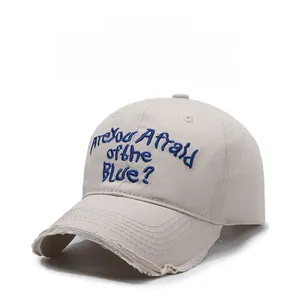 Detail of frayed edge texture and blue embroidery on a beige cotton baseball cap