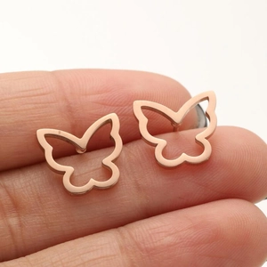 Macro detail of rose gold butterfly earrings displayed on fingers showing texture